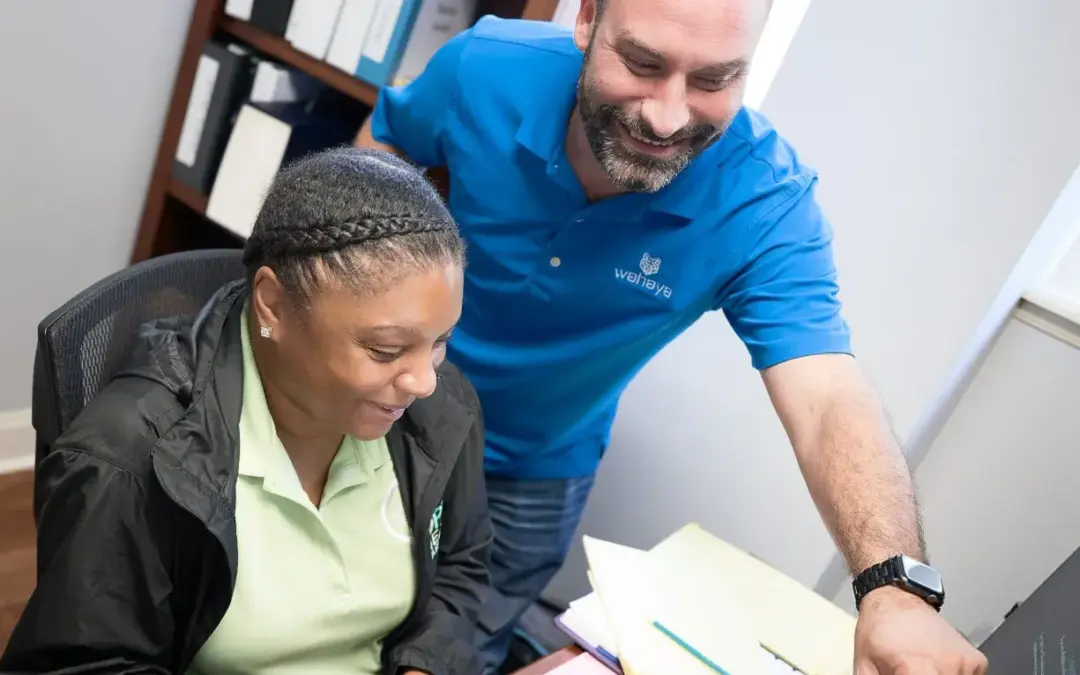 Two professionals collaborating at a desk, one pointing at a computer screen.