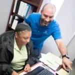 Two professionals collaborating at a desk, one pointing at a computer screen.