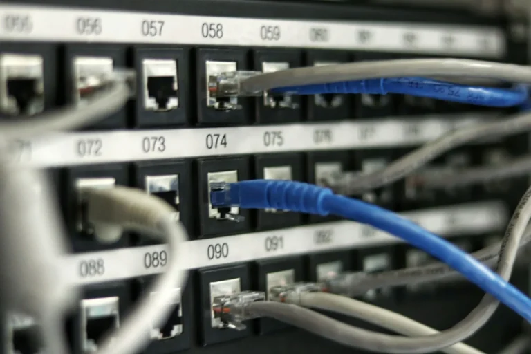 An IT technician reviewing a vulnerability scan report on a laptop next to a network rack