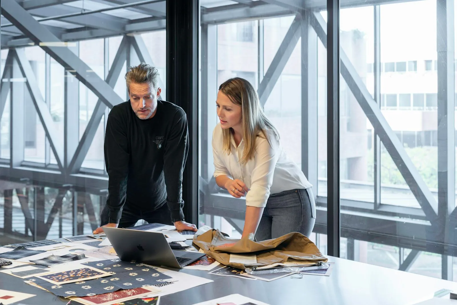 Two coworkers reviewing plans at a table by a window