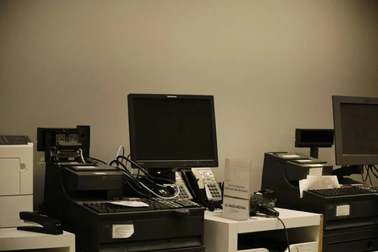 A stack of older laptops next to a new laptop being set up on an office desk