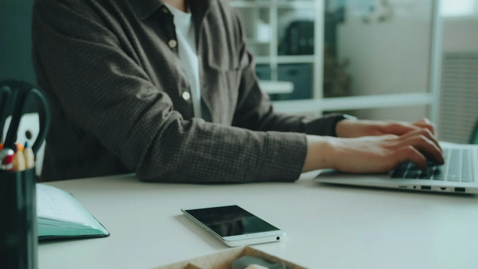 An employee at a desk using a personal smartphone next to a work laptop