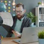 Small business owner at a desk reviewing printed policies next to a laptop