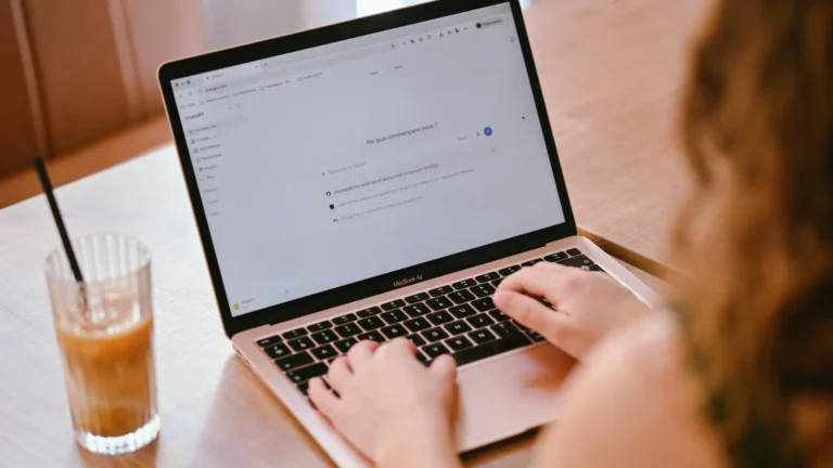 Employee typing on a laptop at a café table with an iced coffee
