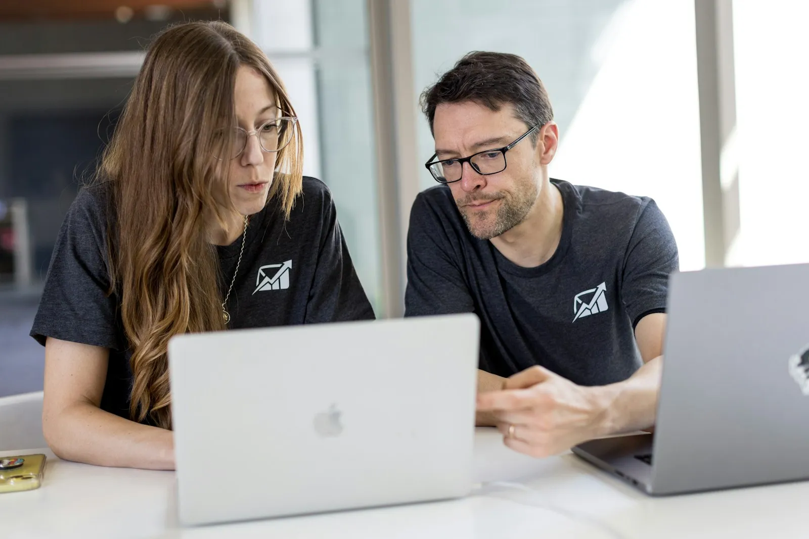 Two volunteers in matching T-shirts working on laptops