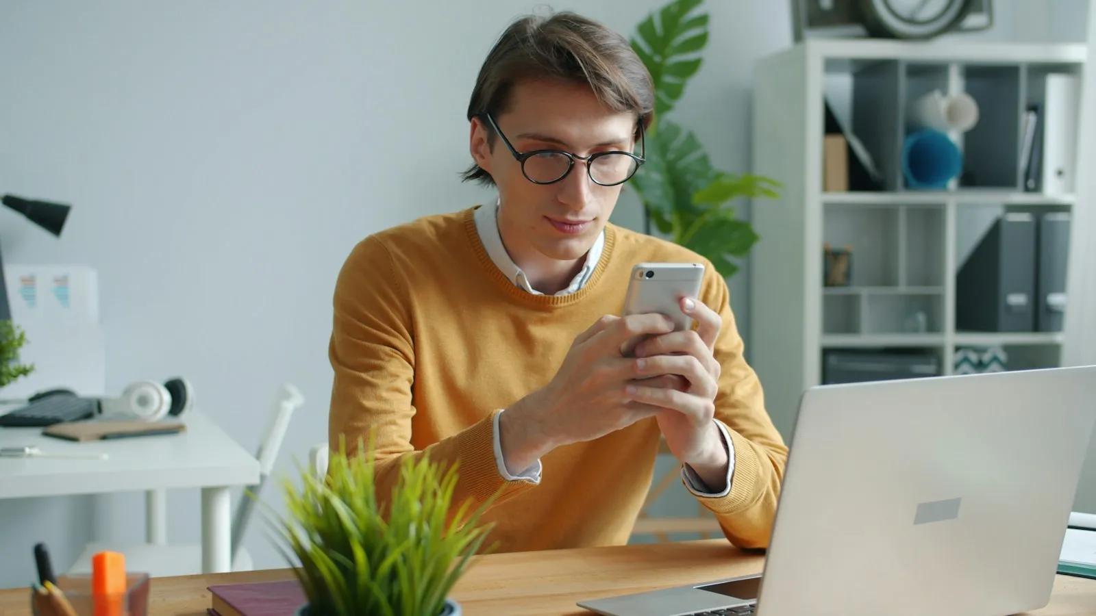 Man in a yellow sweater checking his phone at a desk