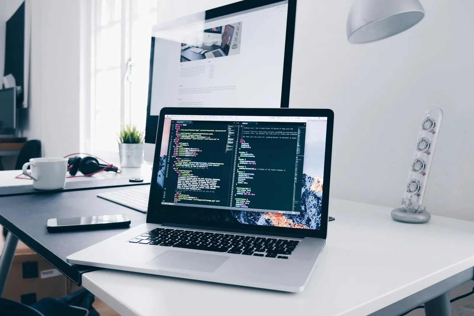 Laptop and monitor with code on a bright desk