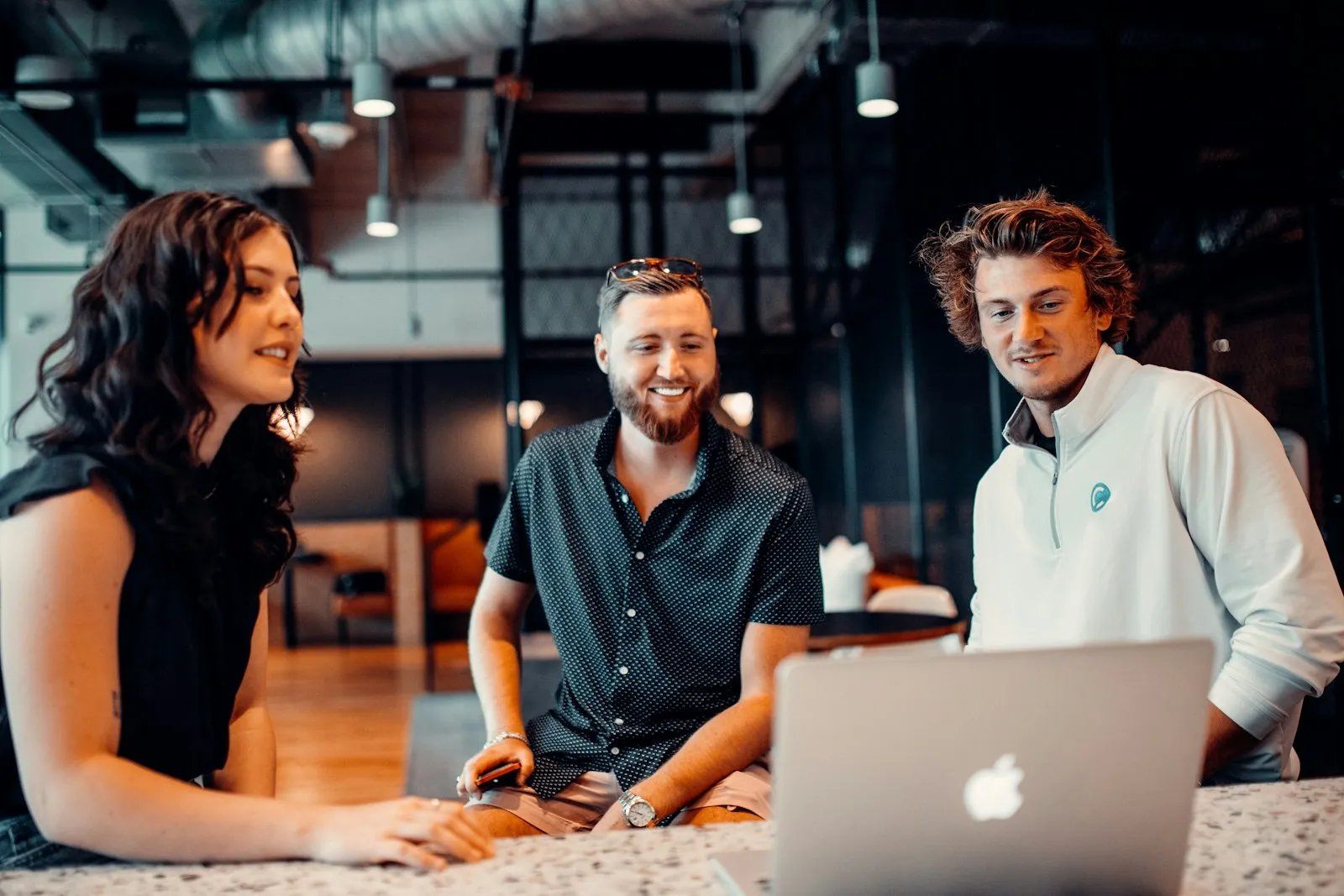 Three coworkers smiling around a laptop