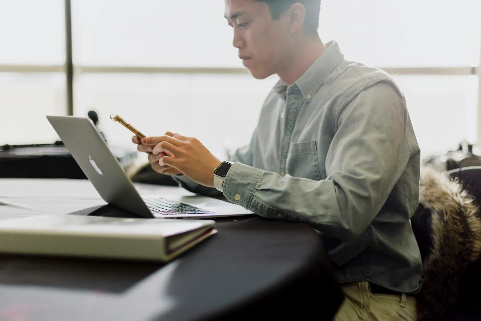 Man checking his phone beside a laptop