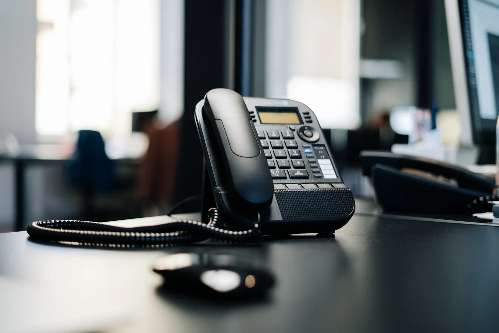 An IP desk phone on an office desk next to a laptop