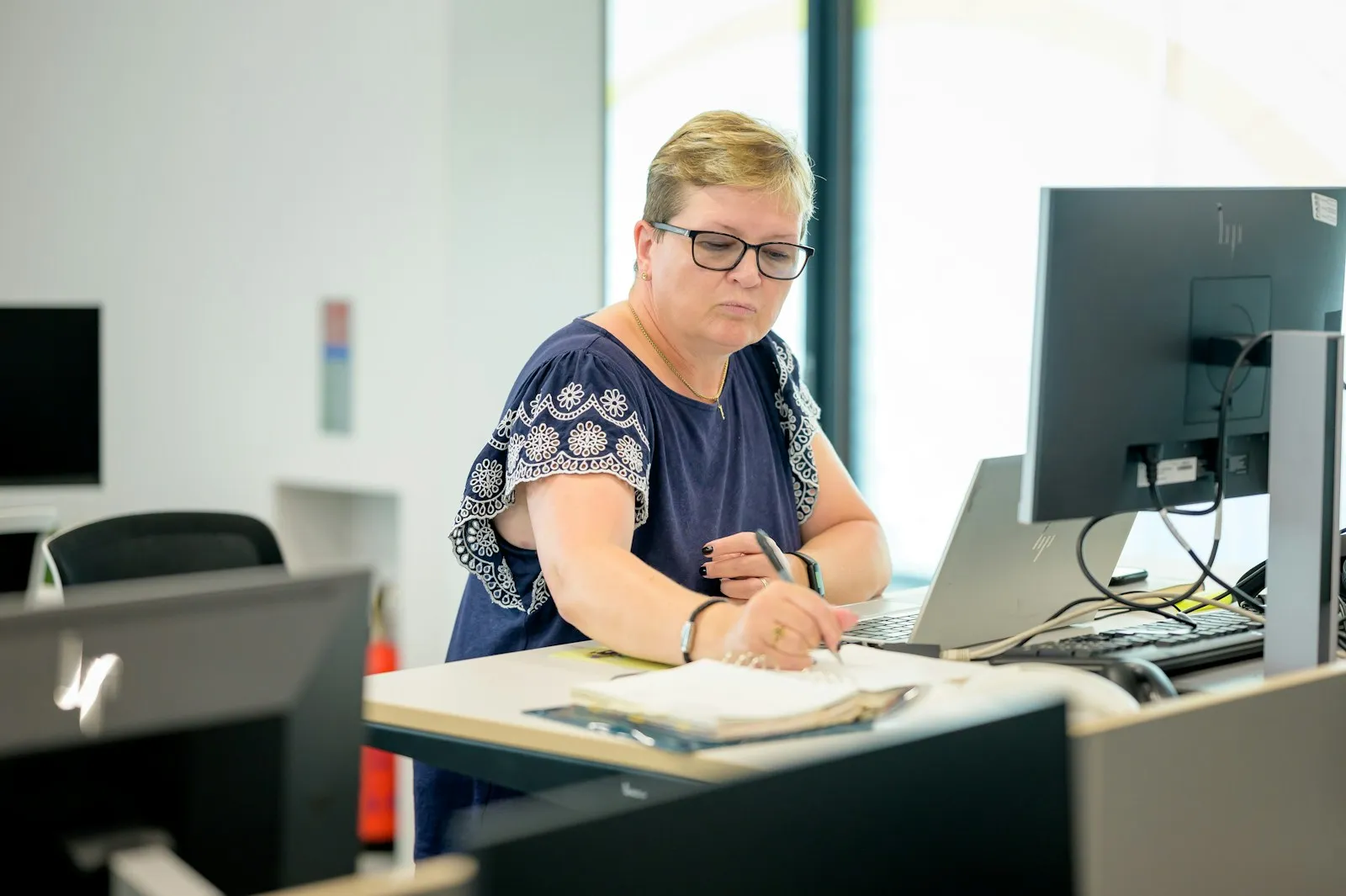 Woman taking notes at her desk beside a computer
