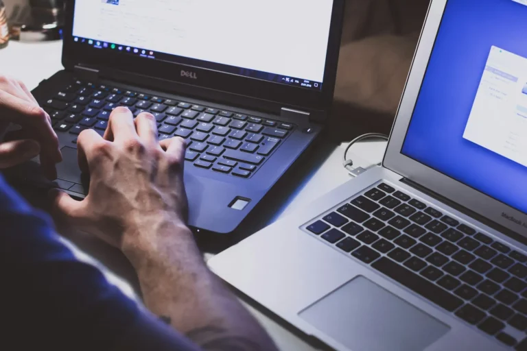 Employee signing in on a laptop while holding a smartphone for a verification prompt